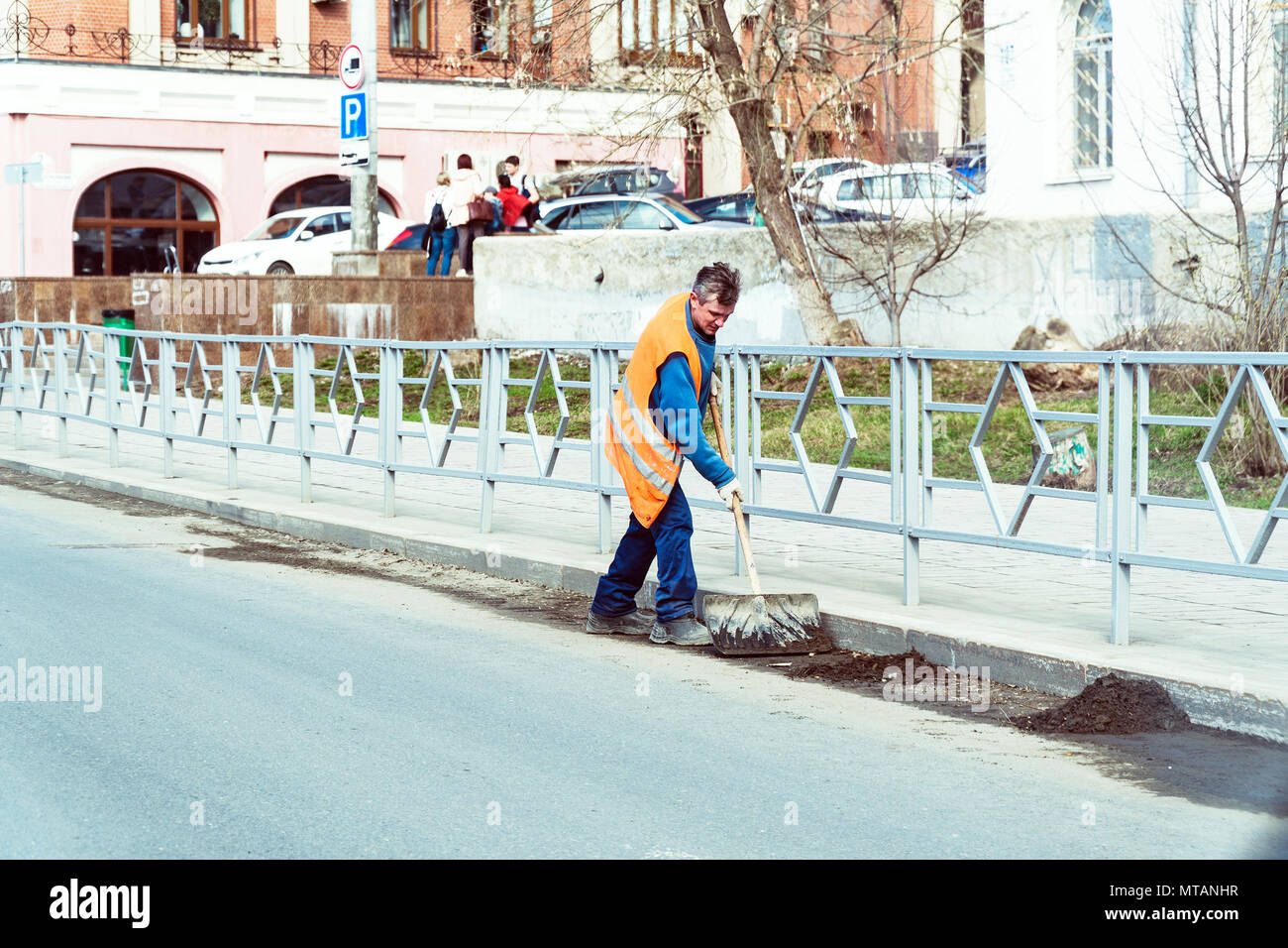 Il bidello in un uniforme arancione pulisce i rifiuti con una pala sulla strada di città Foto Stock