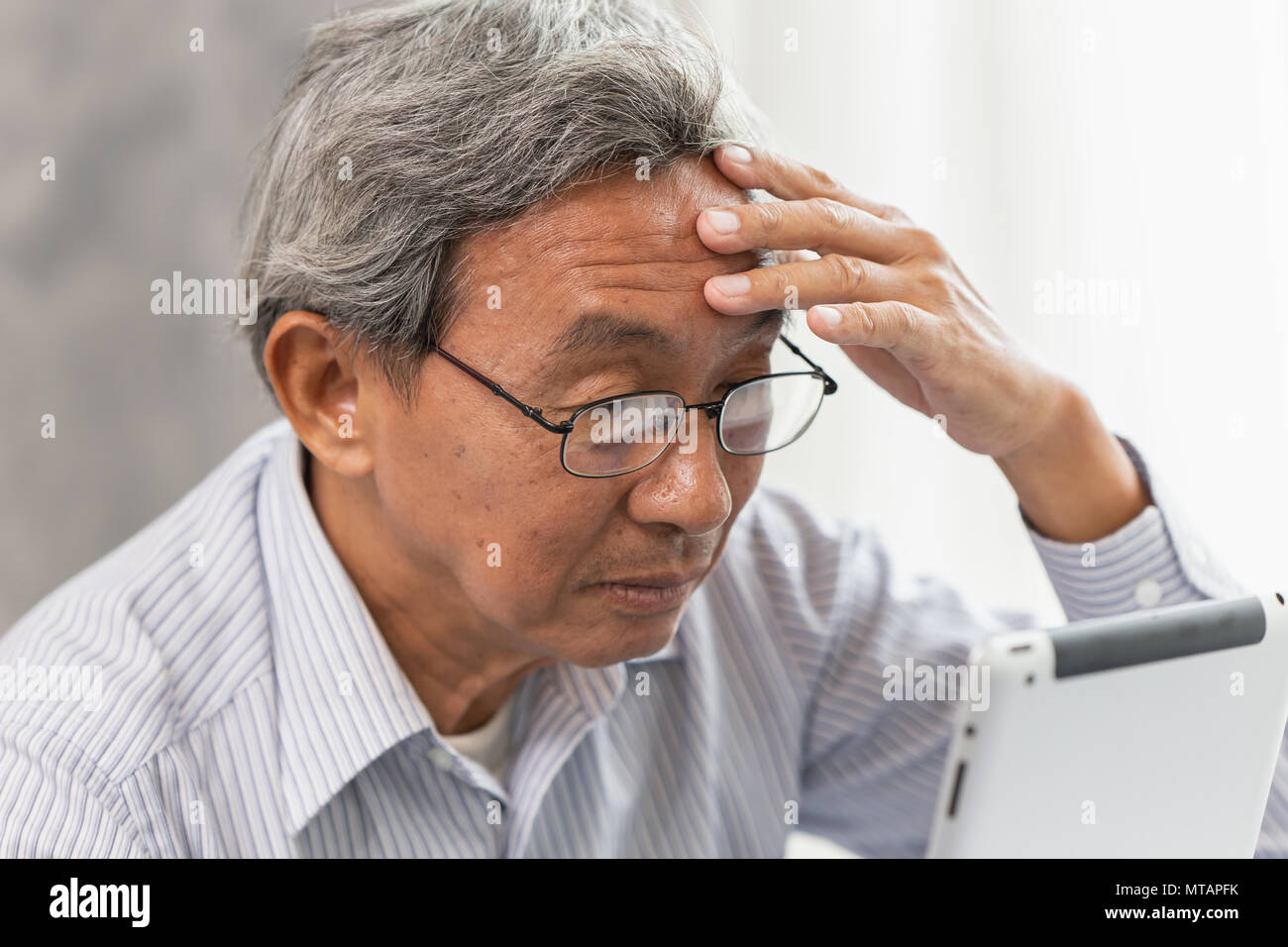 Senior Asian vecchio uomo bicchieri cefalea da uso e guardando lo schermo tablet Foto Stock