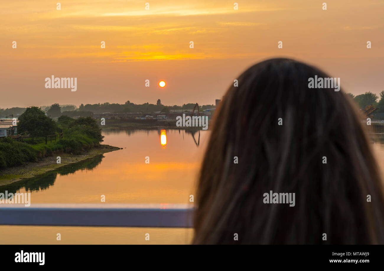 Una donna a guardare il sole andare giù su di un fiume in estate nel Regno Unito. Foto Stock