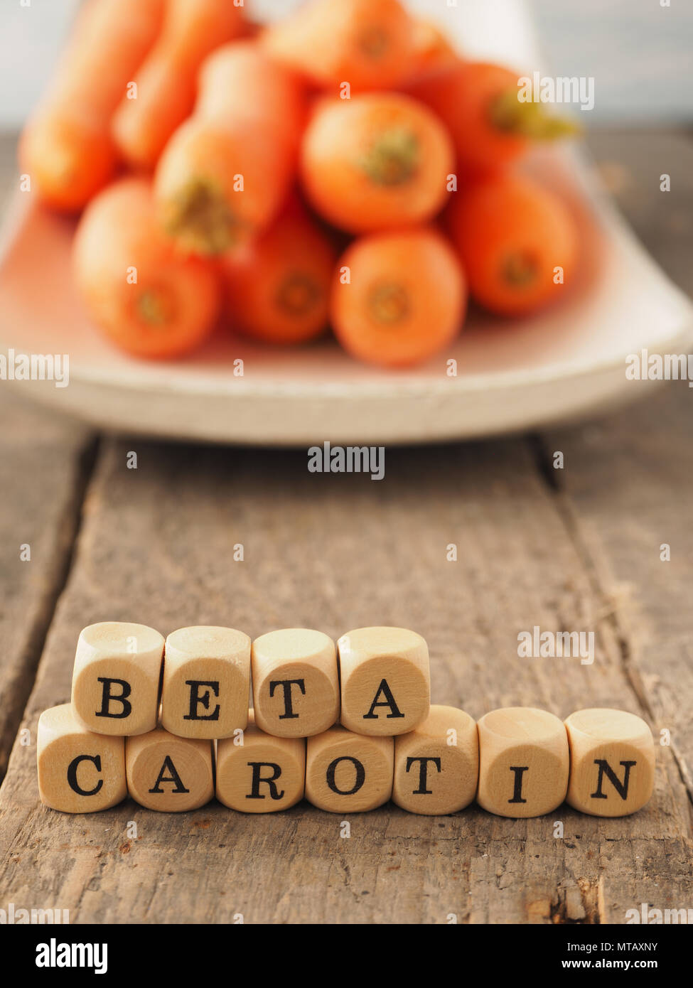 Dadi di legno con le parole tedesche il beta-carotene e le carote fresche nel retro, mangiare sano concetto Foto Stock