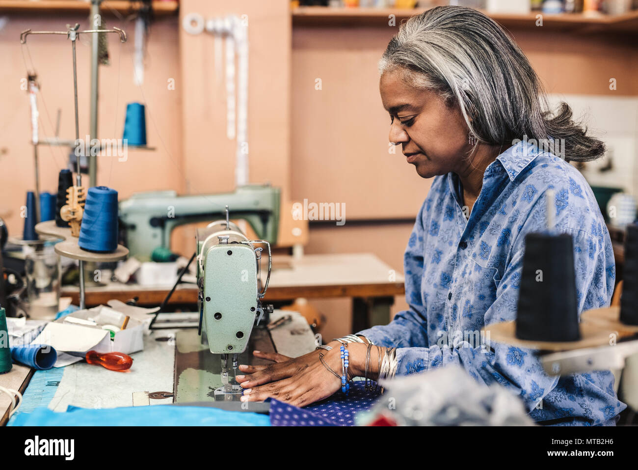 Coppia sarta seduta a una macchina di cucitura Cucitura di un pezzo di tessuto colorato mentre si lavora nel suo negozio Foto Stock