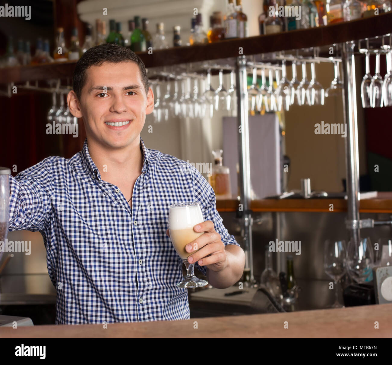 Sorridente bello barista in piedi dietro il bancone bar e h Foto Stock