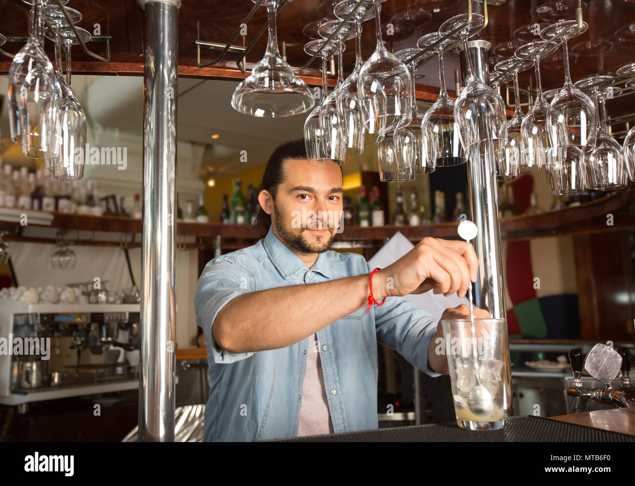 Bel giovane barista sorridente tenendo in acciaio cucchiaio swizzle in Foto Stock