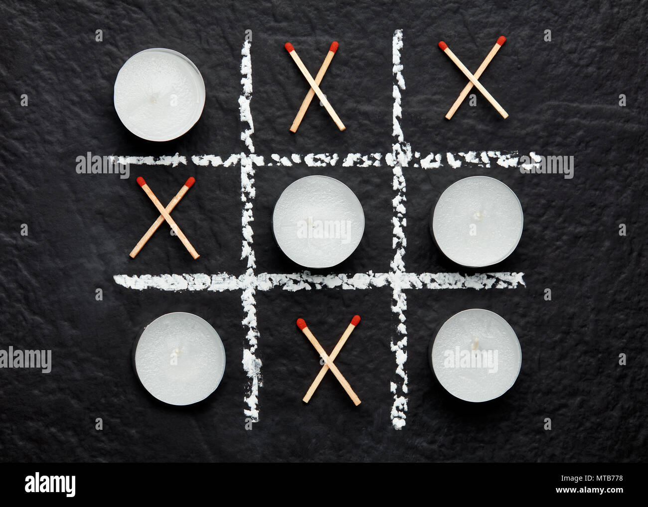 Tic Tac Toe xo gioco con candele e fiammiferi a trama sulla superficie nera. Concetto di fare o di morire e di vita o di morte. Top down vista ravvicinata. Foto Stock