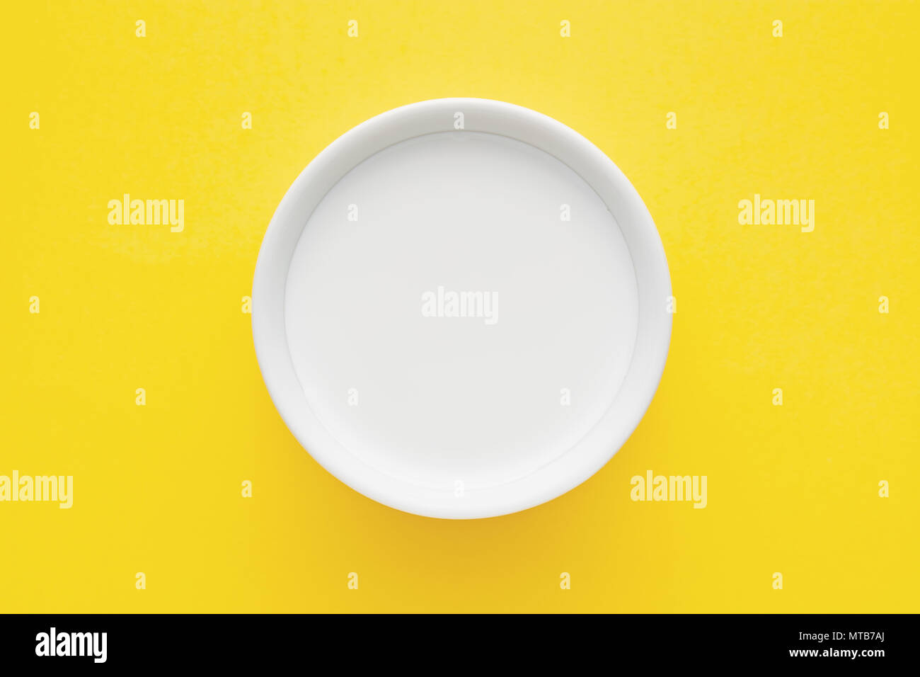 Top down vista minimalista di latte in un recipiente bianco su sfondo giallo Foto Stock