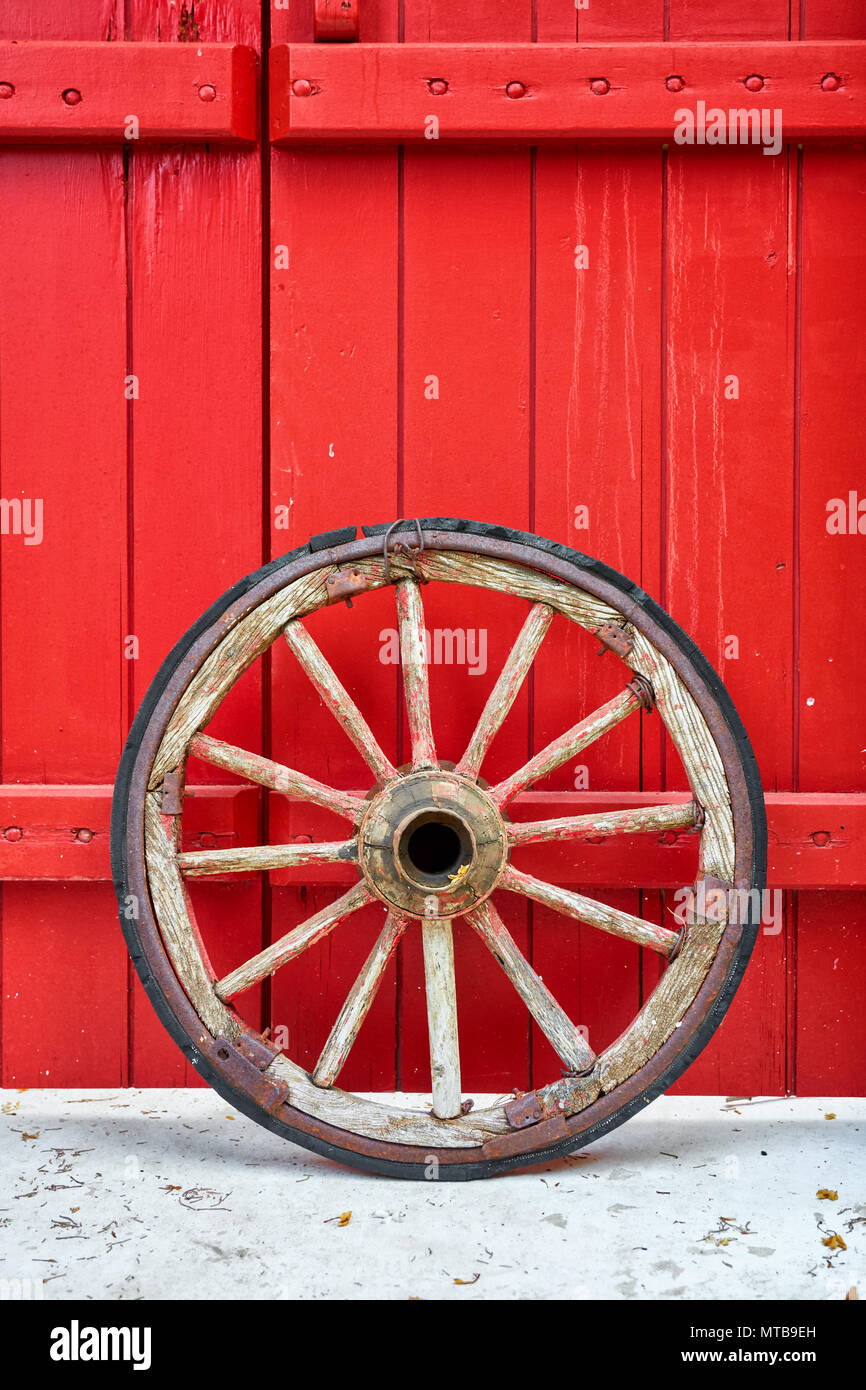 Antique vintage ruota in legno reclinato per un rosso porta in legno Foto Stock