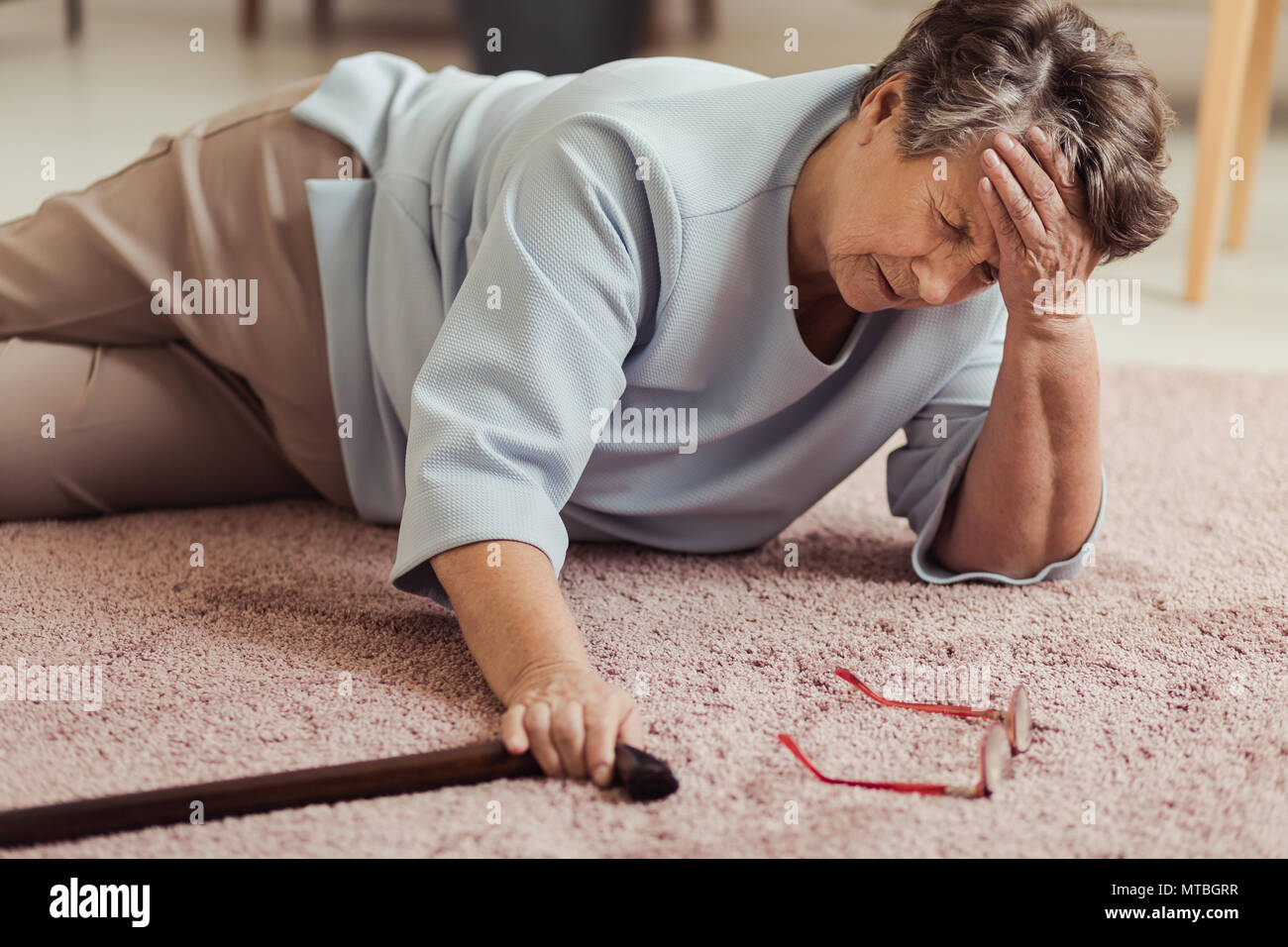 Malati senior donna con mal di testa sdraiato sul pavimento dopo la caduta verso il basso Foto Stock