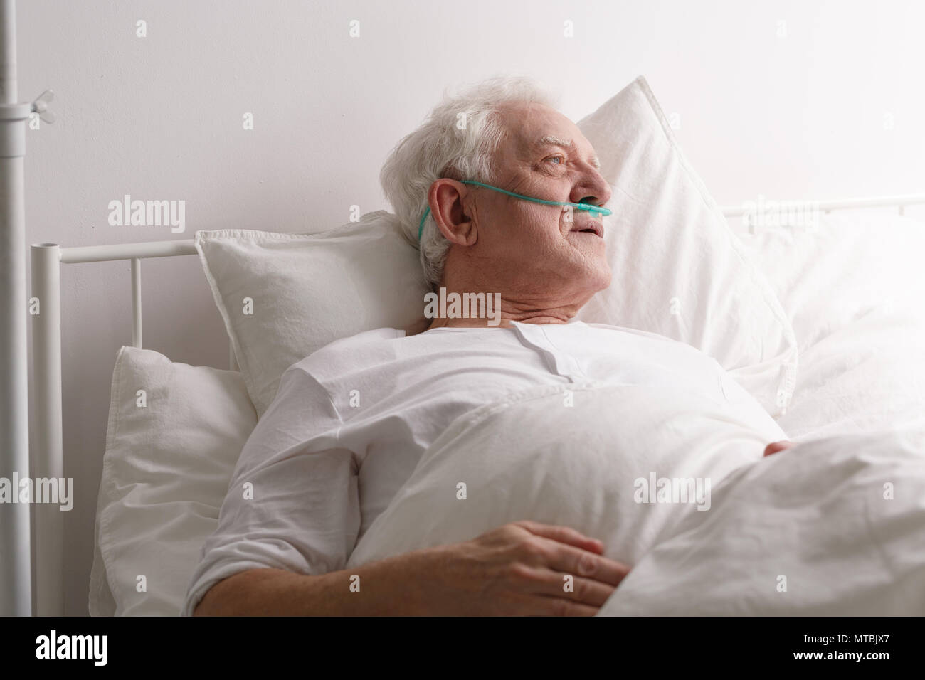 Gli anziani malati morenti uomo nel letto di ospedale a guardare fuori dalla finestra Foto Stock