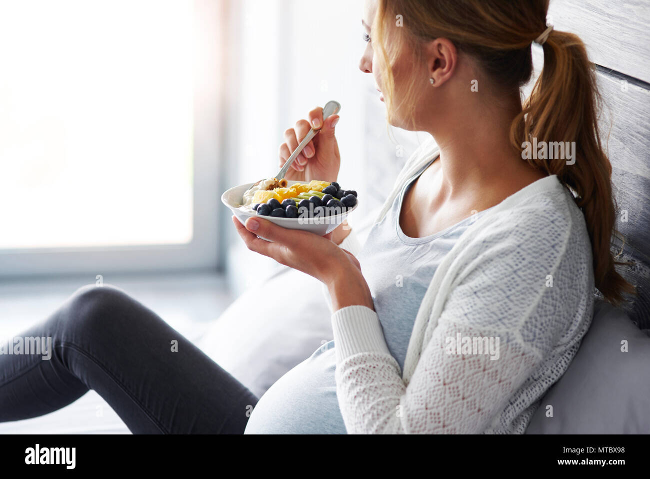 Vista laterale della donna incinta di fare colazione in camera da letto Foto Stock