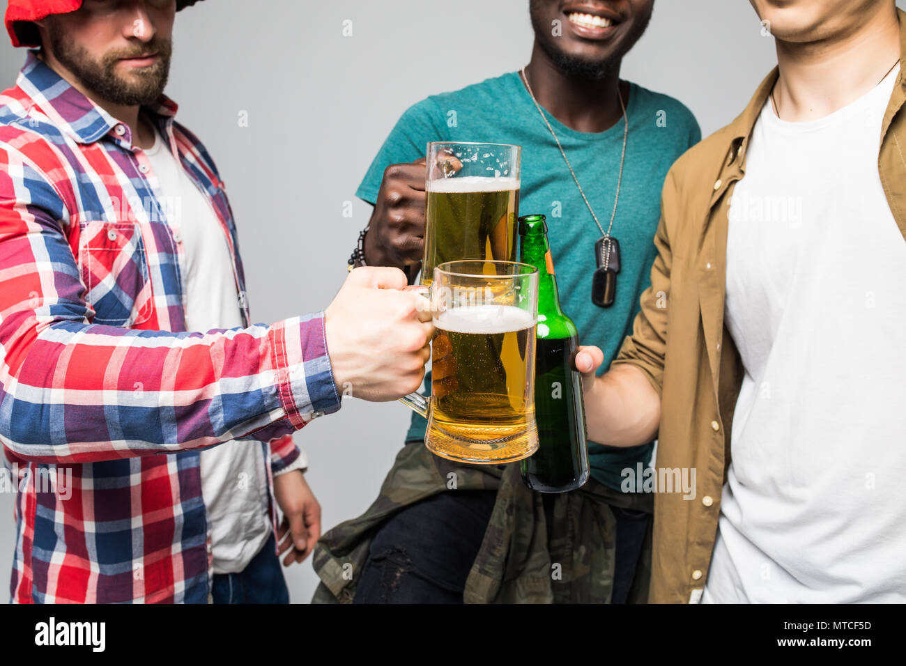 Chiudere fino a tre giovani felici uomini tintinnanti con bicchieri di birra isolato su grigio Foto Stock