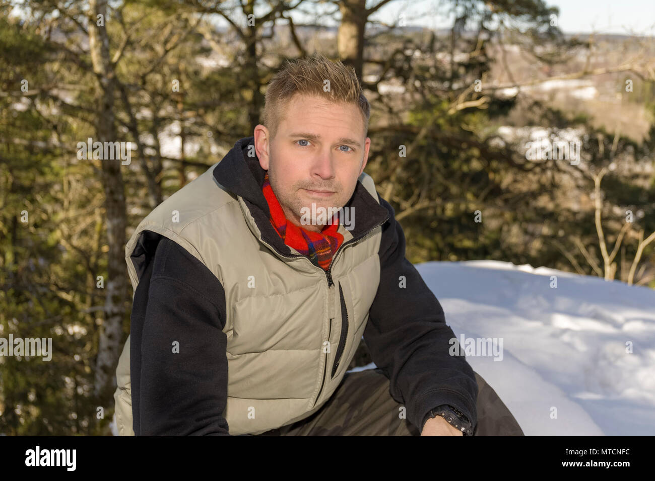 Ritratto di metà adulto 40s uomo caucasico seduti all'aperto nella neve in inverno guardando sorridente della fotocamera Foto Stock