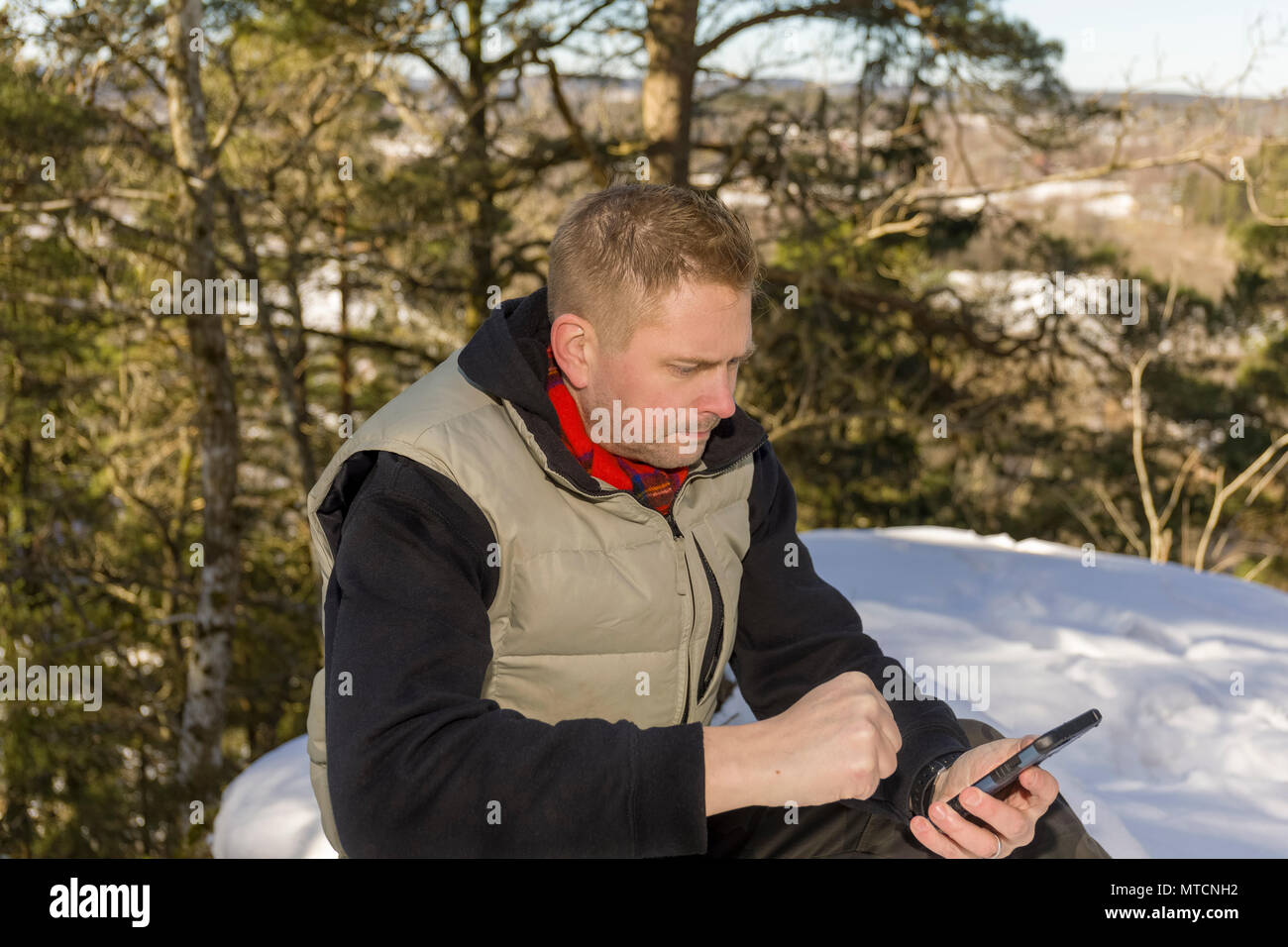 Adulto medio 40s uomo caucasico seduti all'aperto nella neve in inverno con il suo smartphone cercando orinato o infastiditi modello di rilascio: Sì. Proprietà di rilascio: No. Foto Stock