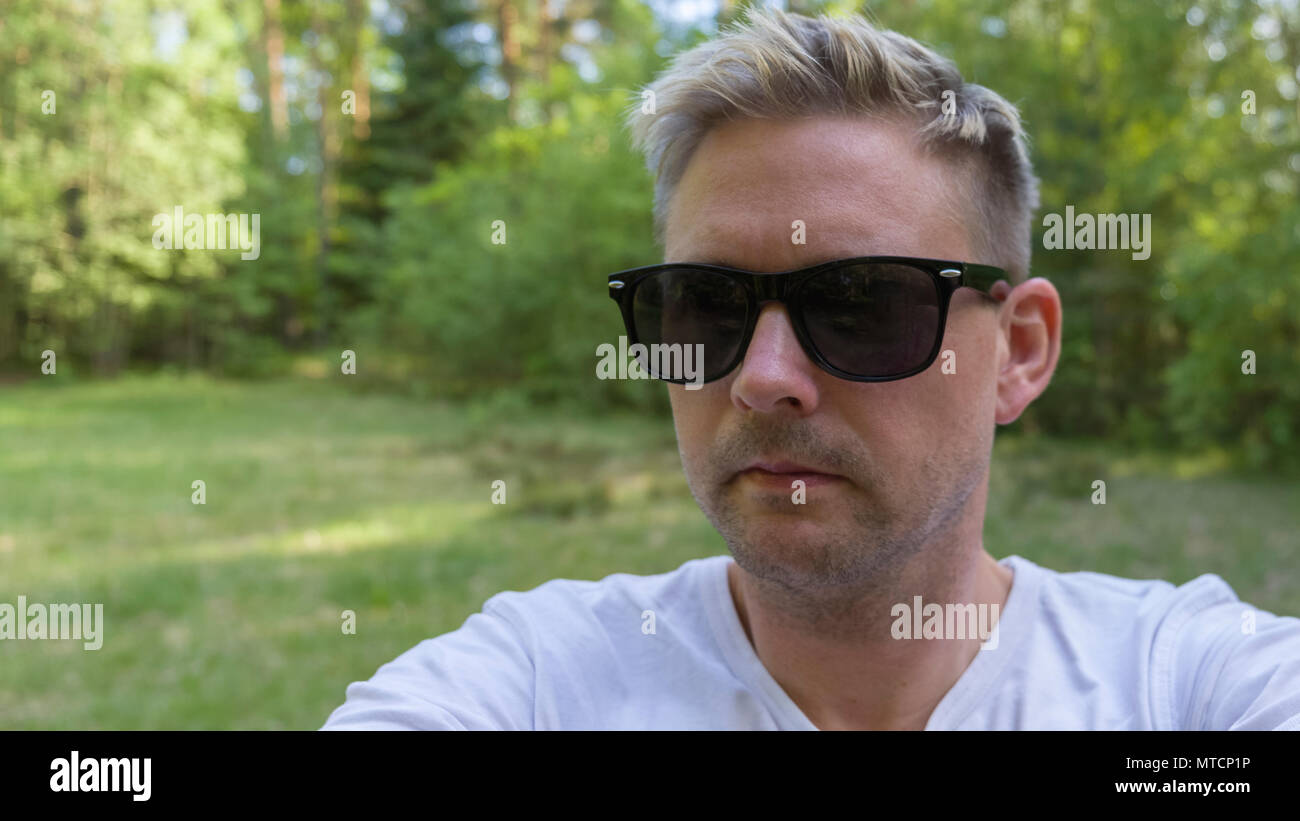 Bello metà adulto 40s uomo caucasico indossando occhiali da sole neri all'aperto in Prato Foto Stock