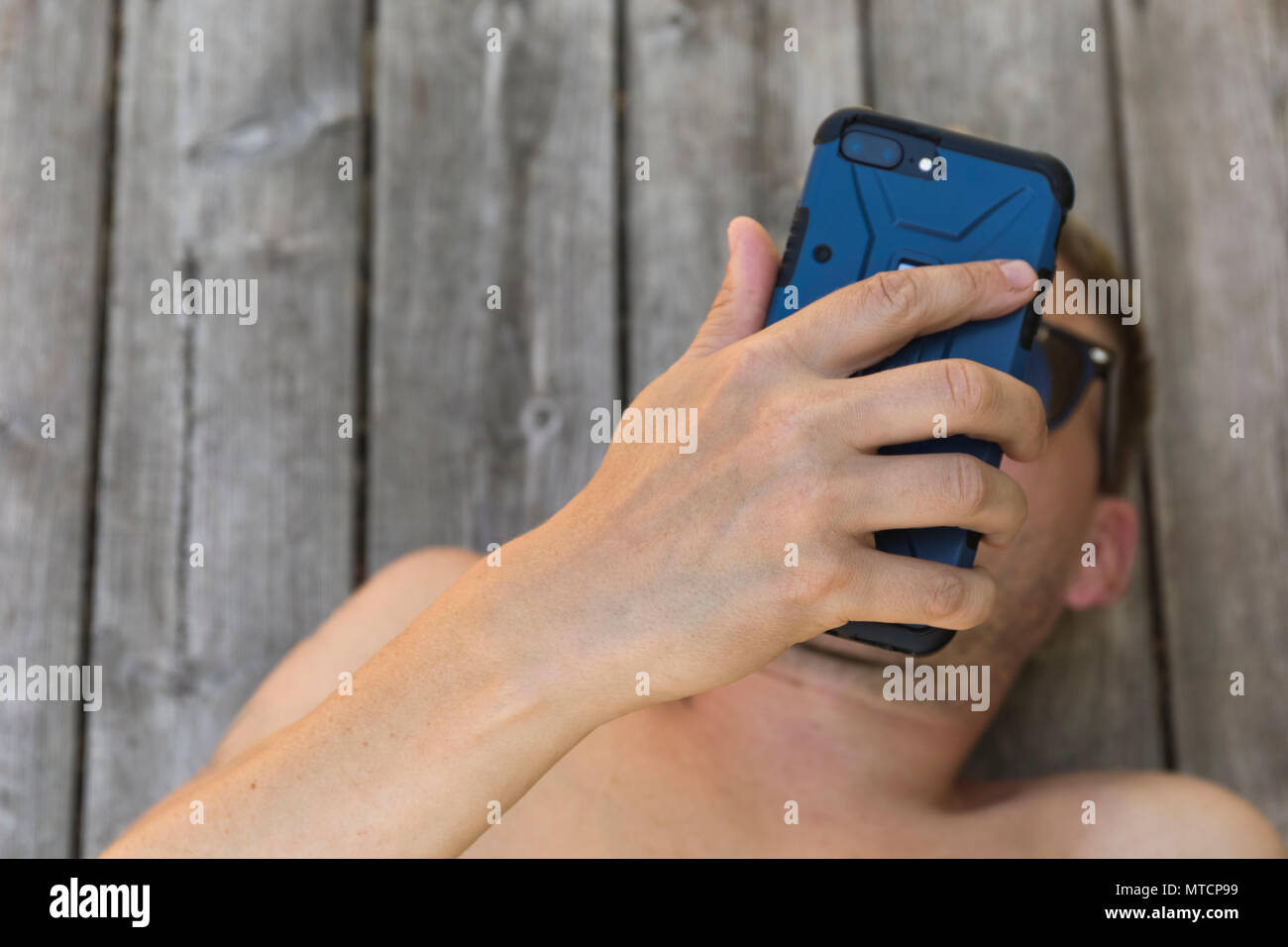 Barechested metà adulto 40s uomo caucasico utilizza lo smartphone telefono cellulare all'aperto sul patio quando vi rilassate in sun Foto Stock