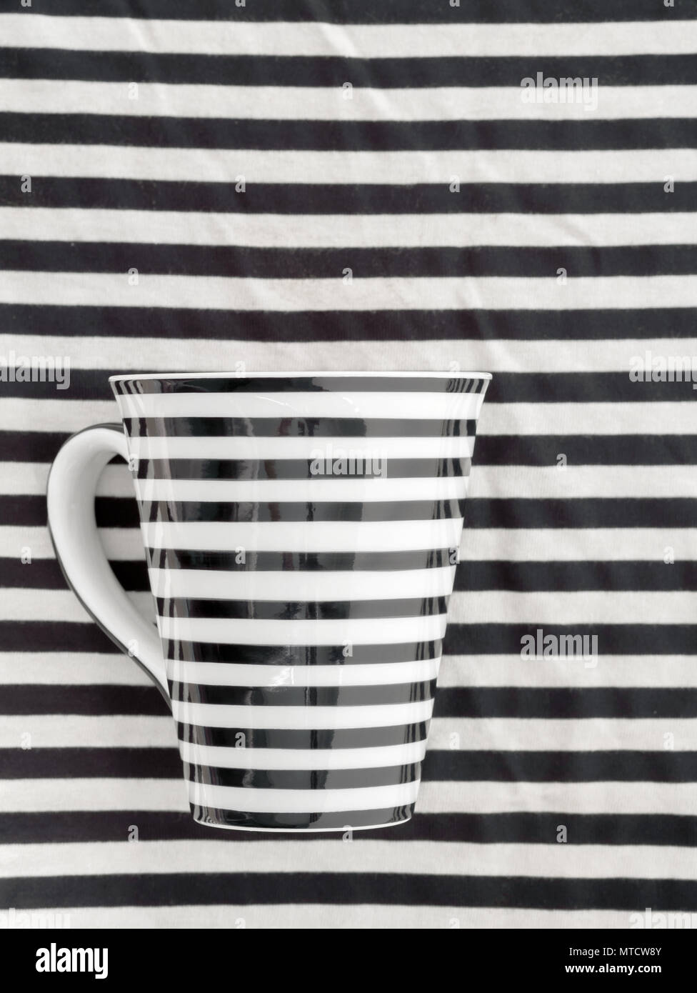 Tazza di ceramica giaceva sul tessuto di strisce in bianco e nero. Vista dall'alto. Lay piatto. Foto Stock