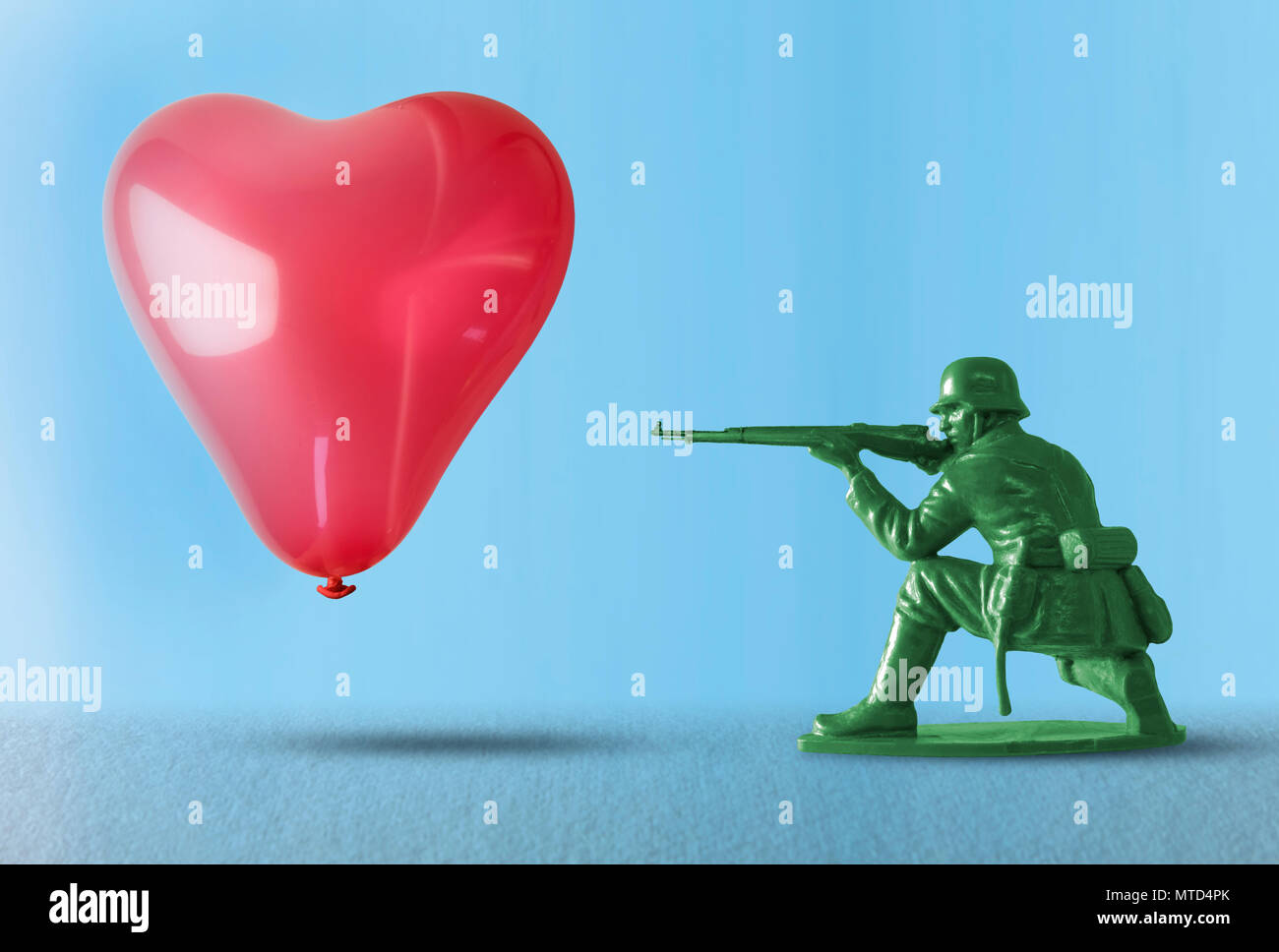 Cuore pallone galleggiante come un bersaglio per un giocattolo soldato con la pistola che rappresentano l'impatto negativo della guerra e della distruzione del flusso di amore con la pistola Foto Stock