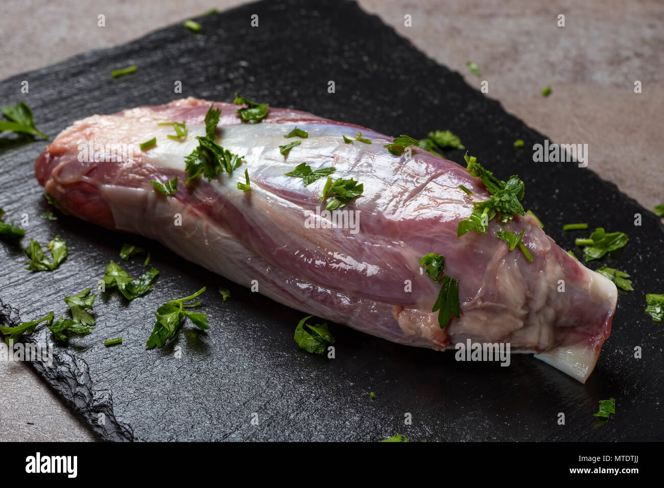 Un nuovo pezzo grezzo della carne di manzo fresco con prezzemolo verde su un di ardesia scura Foto Stock