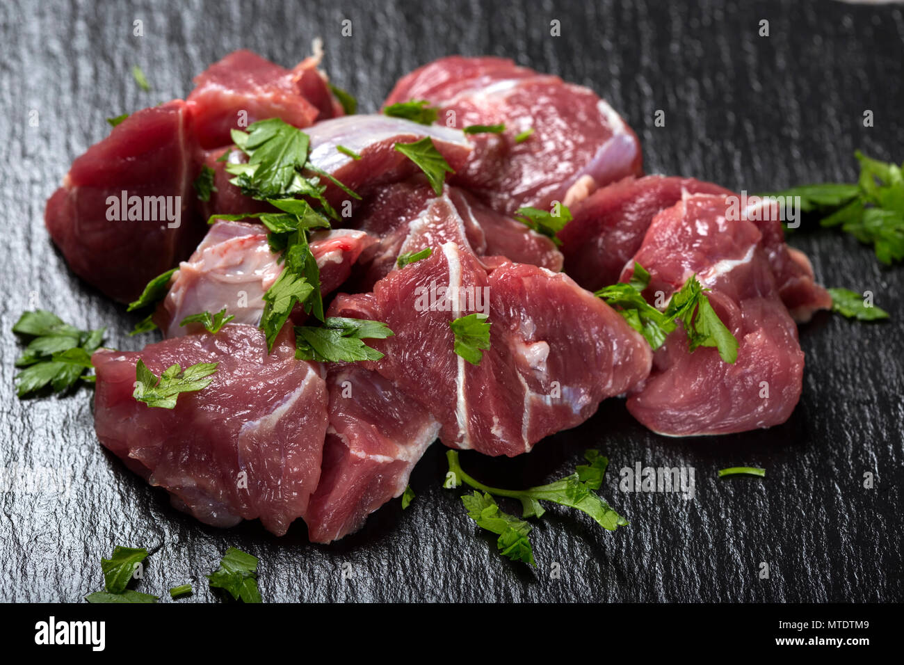 Pezzi di materie di carni bovine al buio su un ardesia con erbe verdi - Vista da vicino Foto Stock