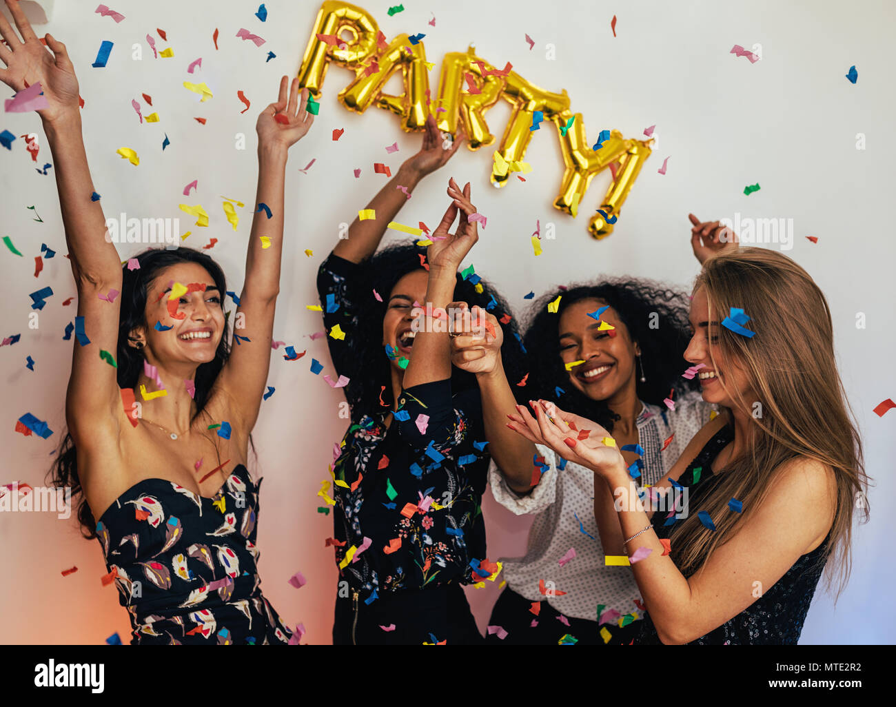 Un gruppo di giovani donne che celebra in interni, gettando coriandoli colorati Foto Stock