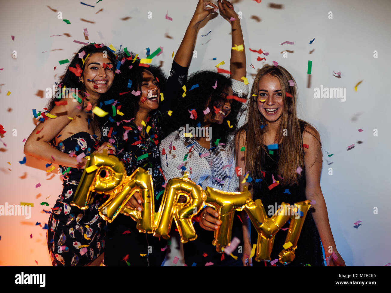 Un gruppo di giovani donne che celebra in interni, gettando coriandoli colorati Foto Stock