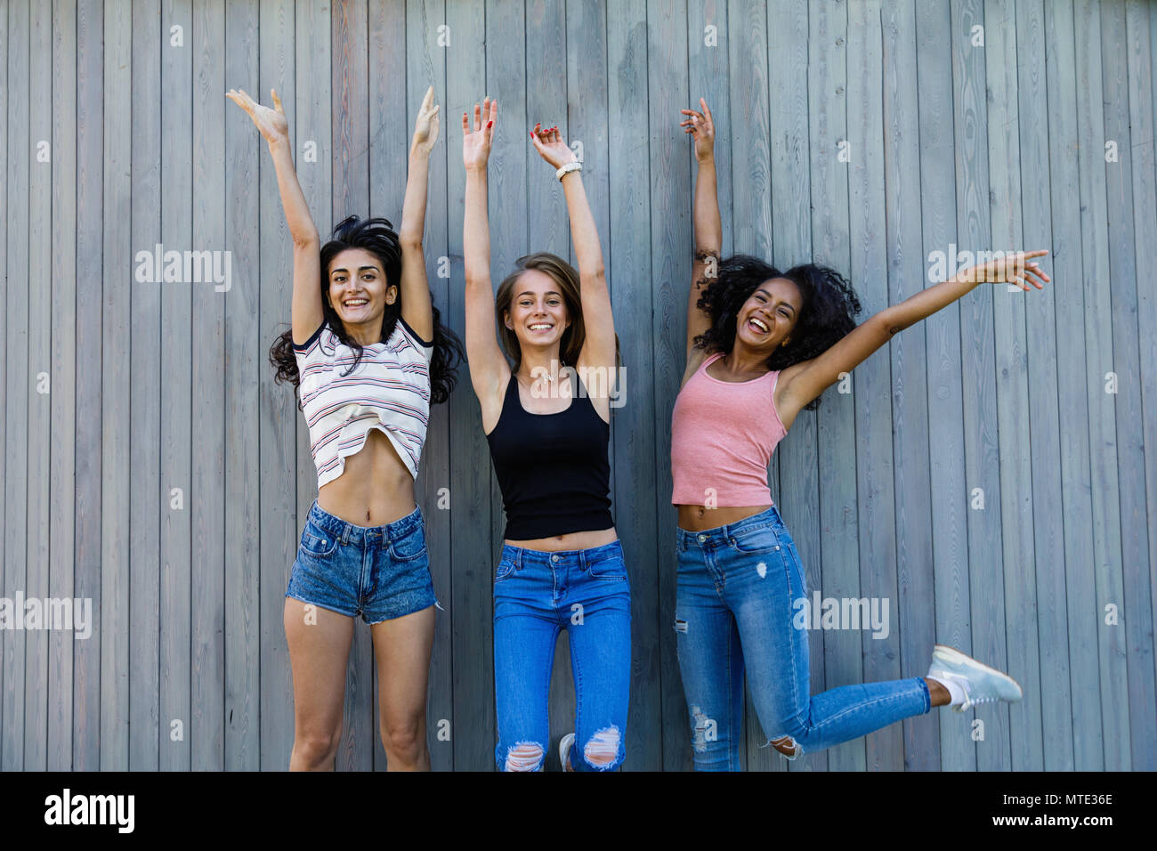 Tre migliori amiche jumping insieme all'aperto vicino a una parete,  guardando la fotocamera Foto stock - Alamy