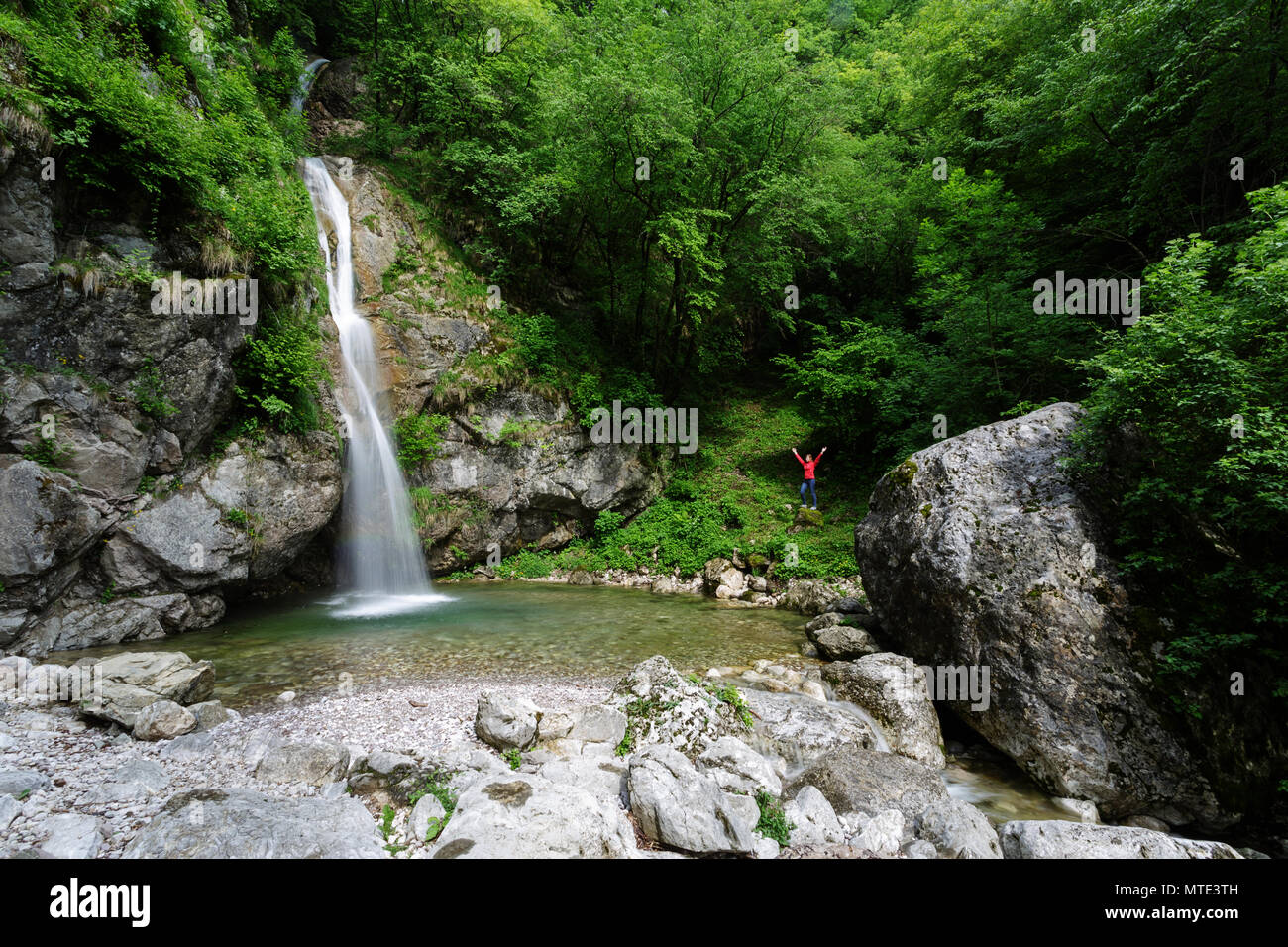 Donna con le mani alzate in piedi in cascata gli schizzi nel pool di smeraldo Foto Stock