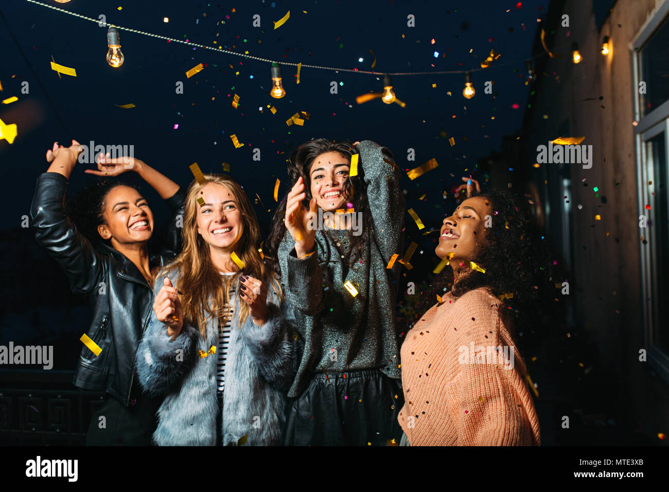Festa notturna su una terrazza. Felici donne divertimento sotto coriandoli. Foto Stock