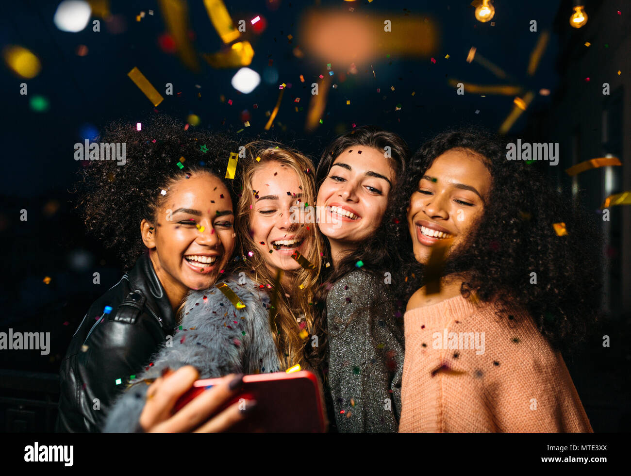 Gruppo di felici donne tenendo selfie sul telefono cellulare, in piedi all'aperto durante la notte Foto Stock