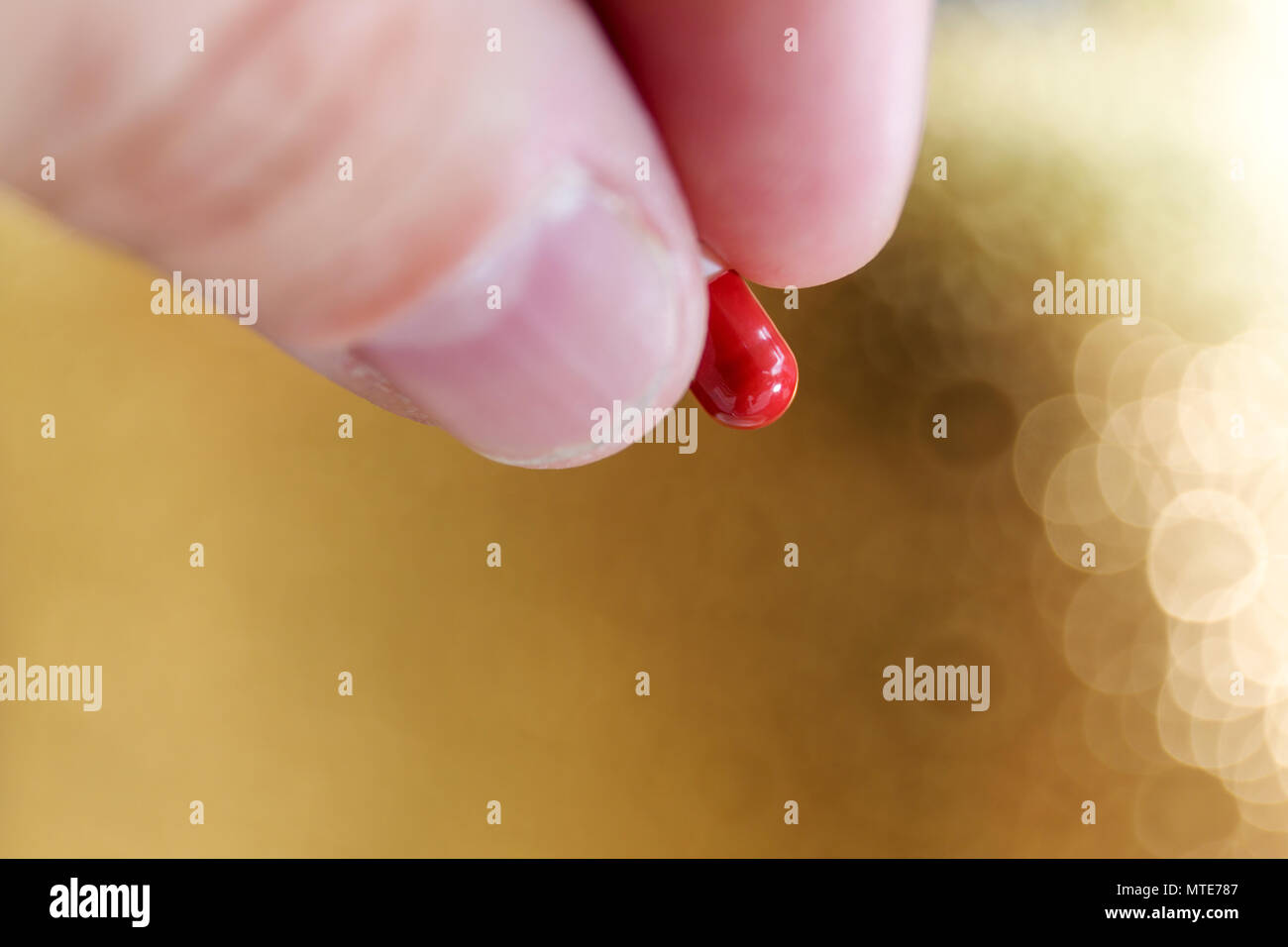 Vista ravvicinata della mano e delle dita holding rosso e bianco medicina di capsula nella parte anteriore del fondo oro Foto Stock