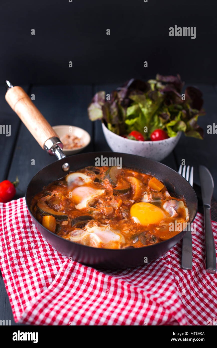 La prima colazione. Uova fritte con verdure - shakshuka in una padella su un sfondo di legno in stile rustico. Lay piatto. Vista dall'alto. Foto Stock