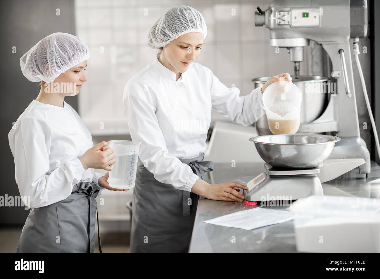 Due femmina pasticceri in uniforme del peso di ingredienti per pasticceria lavorando presso la pasticceria La fabbricazione Foto Stock