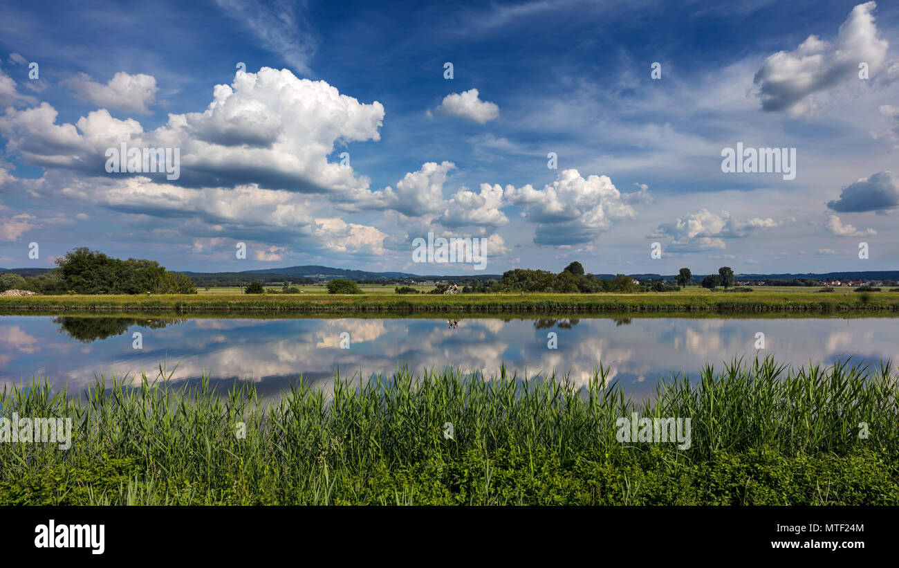 Drammatica nuvole nel cielo blu riflettono nell'acqua del canale Reno-Meno-Danubio vicino a Forchheim in Germania. Foto Stock
