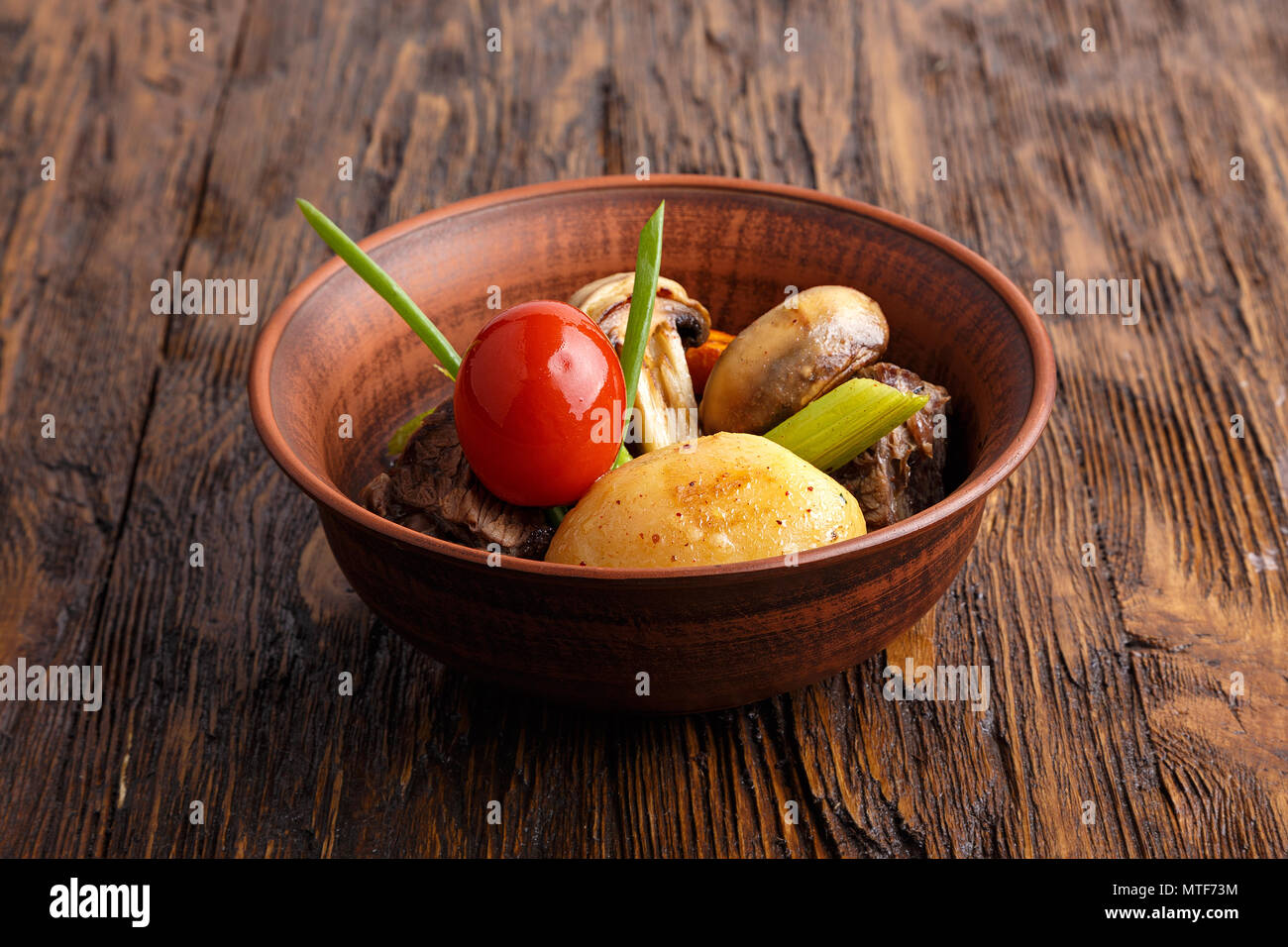 Stufato di carne con verdure in un tegame di coccio. funghi, carote, pomodori, sedano, cipolla. orizzontale Foto Stock
