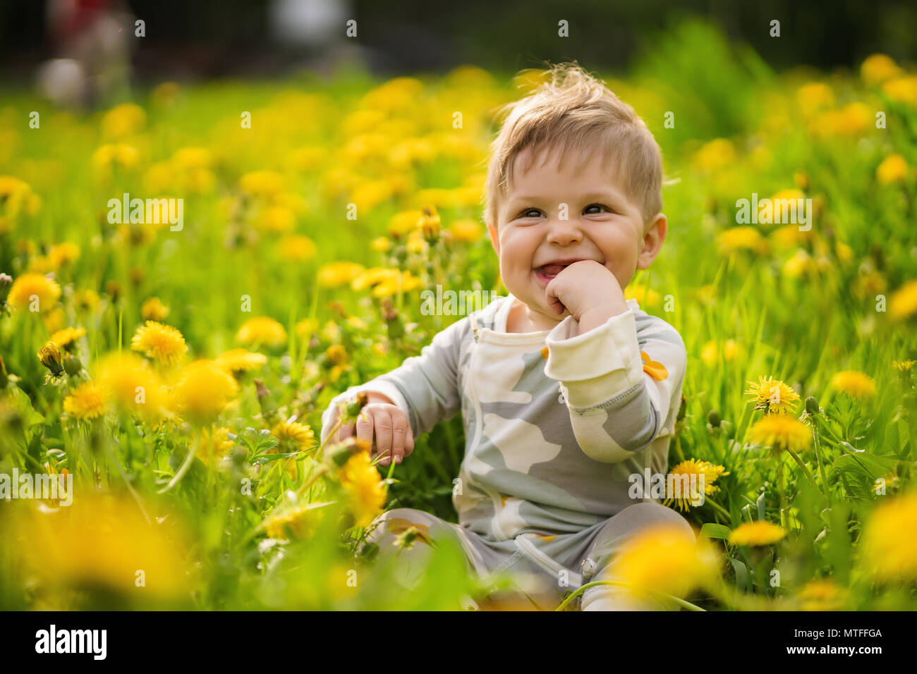 Concetto: i valori della famiglia. Ritratto di Innocenzo adorabili brown-eyed baby giocare all'aperto nel soleggiato Campo di tarassaco e facendo facce buffe. Foto Stock