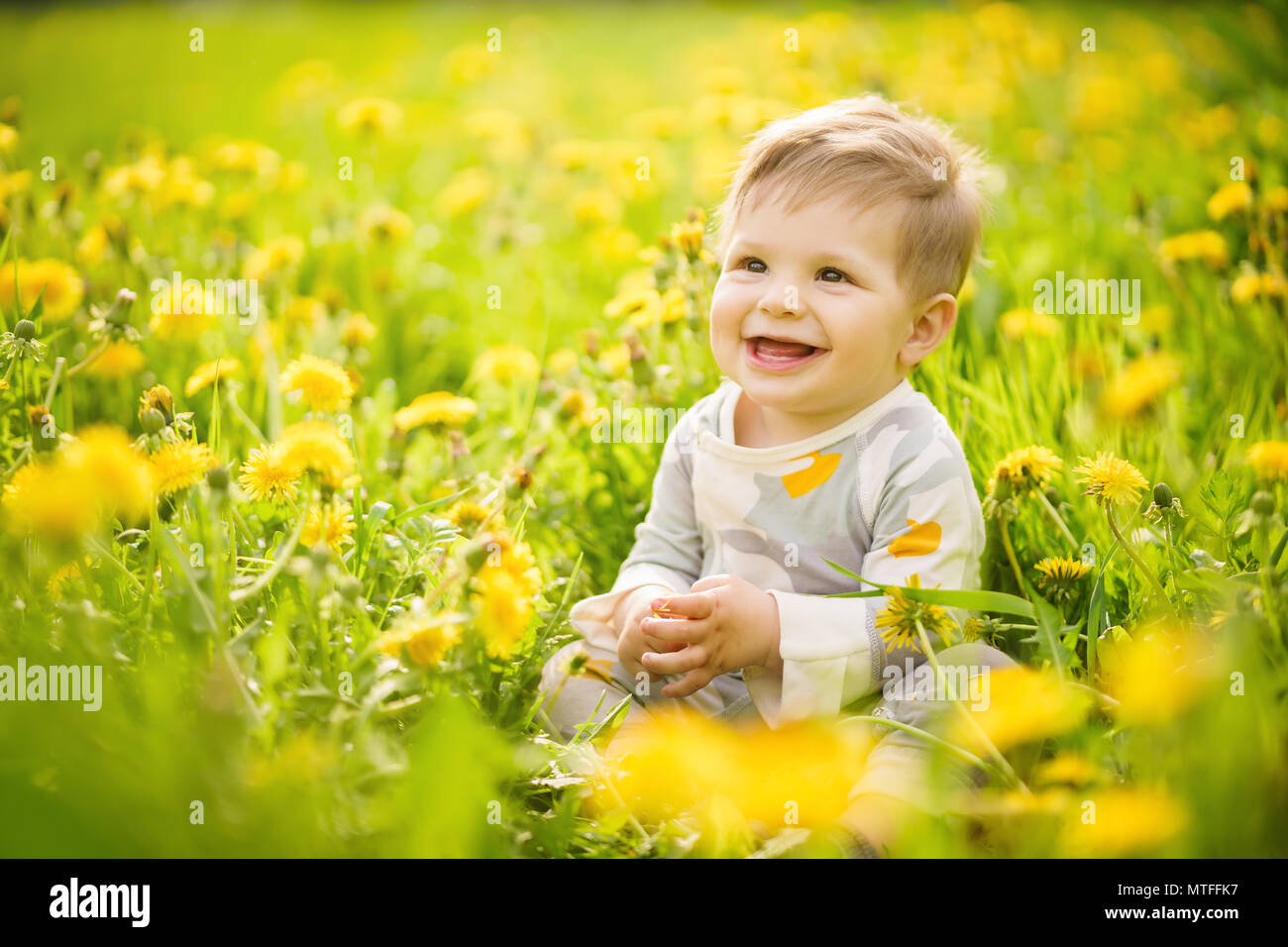 Concetto: i valori della famiglia. Ritratto di Innocenzo adorabili brown-eyed baby giocare all'aperto nel soleggiato Campo di tarassaco e facendo facce buffe. Foto Stock