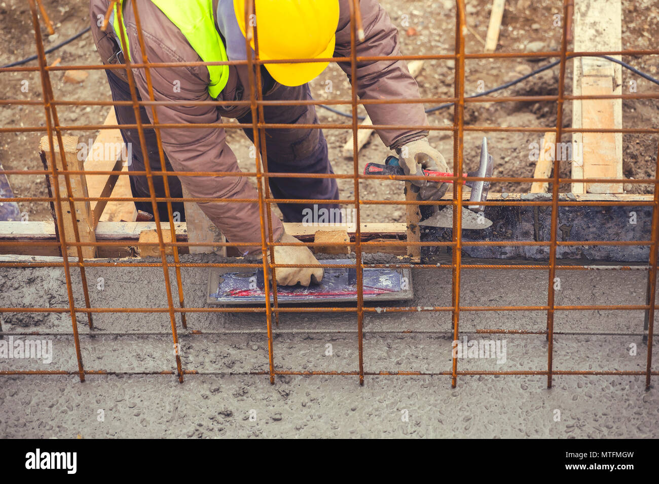 Builder utilizzando cazzuola di finitura per livellamento e buon calcestruzzo bagnato. Basamento in cemento pour con tondino e cassero. In stile vintage. Foto Stock