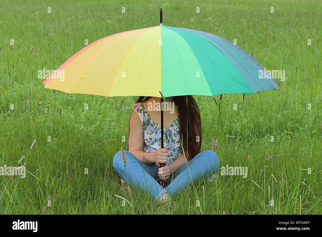 Femmina è seduto sotto colorati ombrello Arcobaleno su erba verde campo. Luminose Foto Stock