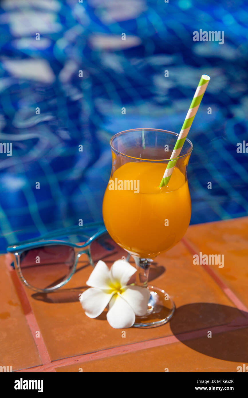 Succo di arancia con gli occhiali da sole sul al bordo della piscina - vacanza concetto tropicale Foto Stock