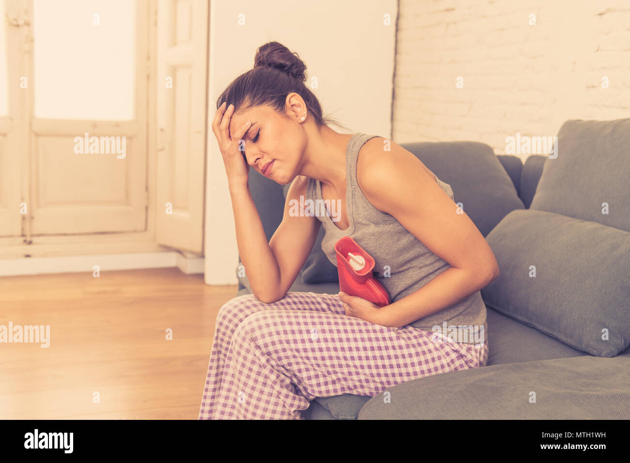 Giovani belle latino donna ispanica nella espressione di dolorosa sofferenza crampi allo stomaco e periodo mestruale dolore tenendo un acqua calda bottiglia contro ventre Foto Stock
