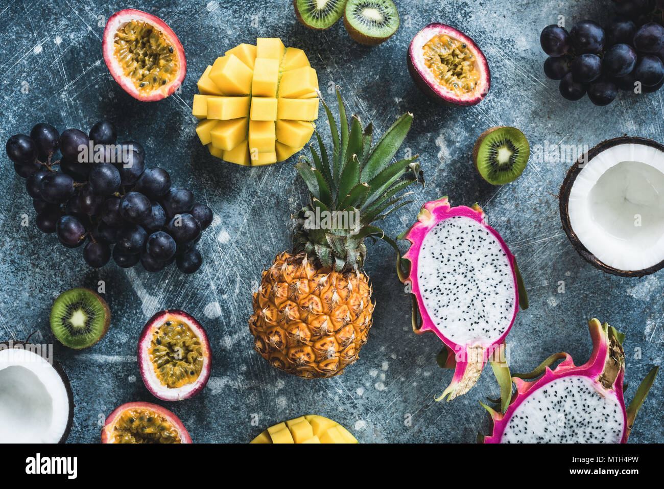 Frutti tropicali, frutti esotici su sfondo di calcestruzzo. Piatto di frutta laici. Dragonfruit, granadiglie, noce di cocco, mango, kiwi e uva. Crudo fresco frutta bac Foto Stock