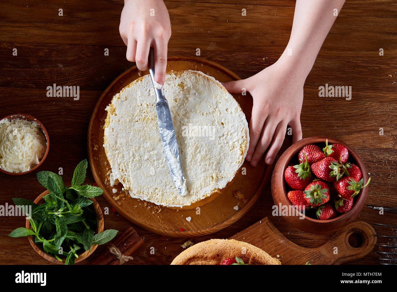 Close up della ragazza con le mani in mano l'aggiunta di un po' di panna di panna acida sulla parte superiore di una deliziosa torta di fragole, il fuoco selettivo. Gustosa pasta è sul tavolo di legno Foto Stock