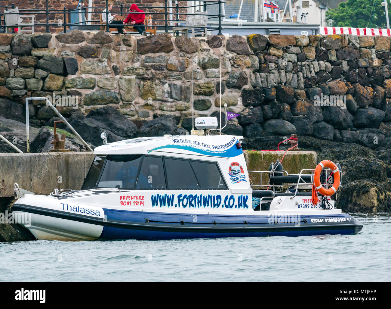 Via Wild Adventure imbarcazione attraccata al molo con coppia giovane seduto su un banco di lavoro, North Berwick, East Lothian, Scozia, Regno Unito Foto Stock