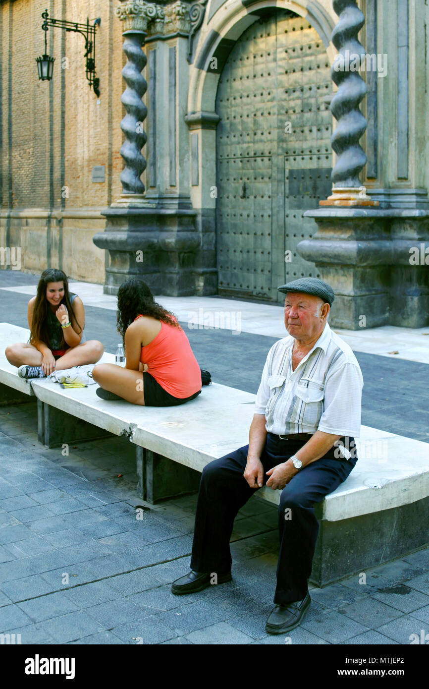 Uomo anziano e due ragazze adolescenti condividono un banco di marmo davanti a una porta di ingresso alla Iglesia de San Felipe / San Felipe Chiesa, Saragozza, Aragona, Spagna Foto Stock