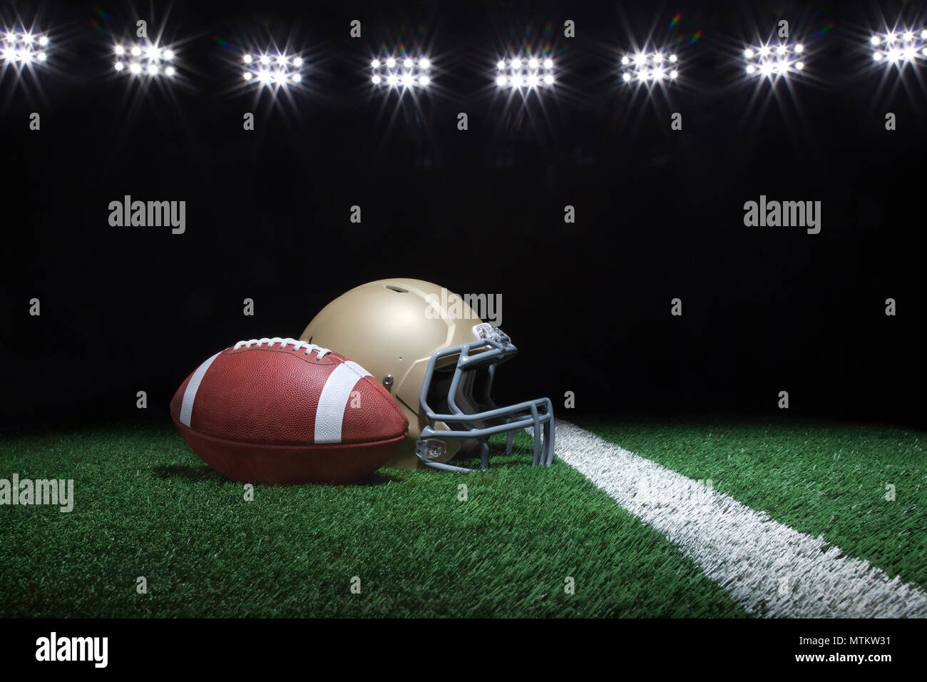 Calcio e casco d'oro sul campo in erba sotto le luci dello stadio di notte Foto Stock