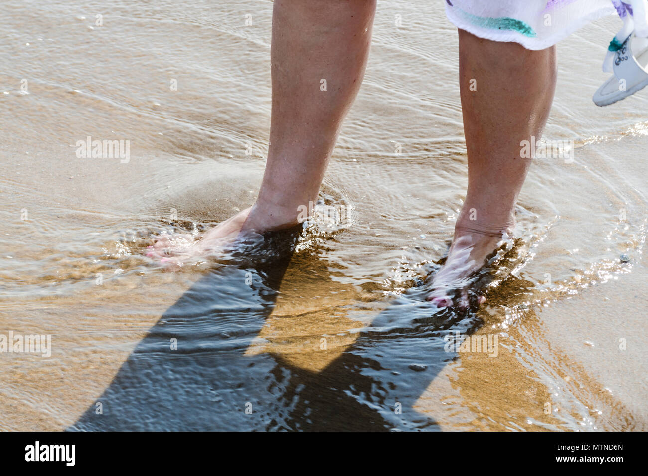 Le donne le gambe in mare in spiaggia con spruzzi di acqua e cadute Foto Stock