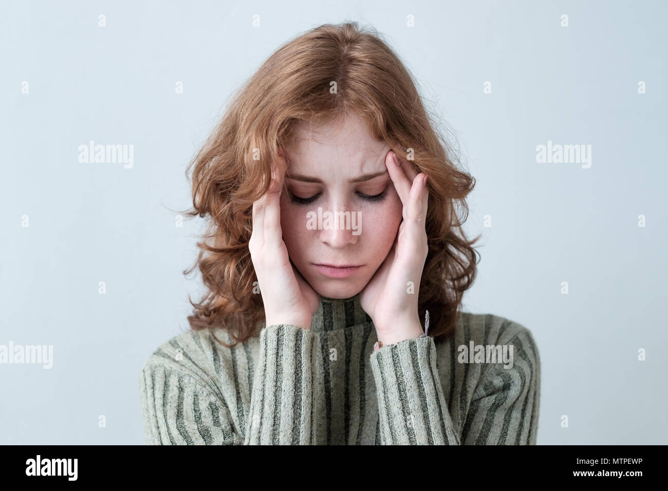 Giovane donna caucasica con red capelli ricci tenendo la testa nel dolore su sfondo bianco. Foto Stock