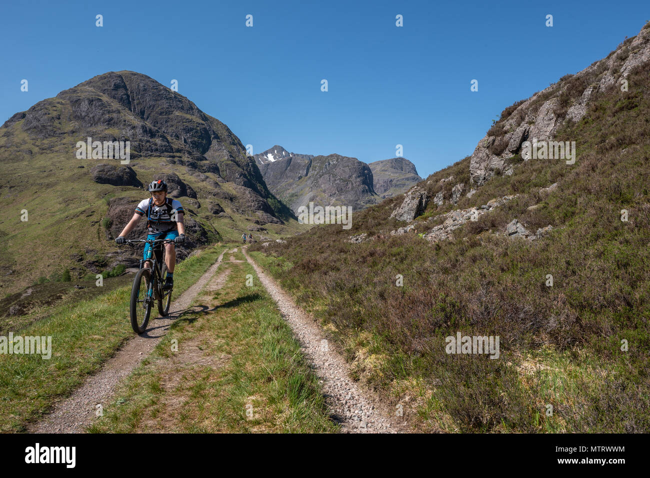 I ciclisti sulla vecchia strada militare sulle colline sopra la nuova strada che corre attraverso Glencoe con la struttura ad albero delle sorelle in background Foto Stock