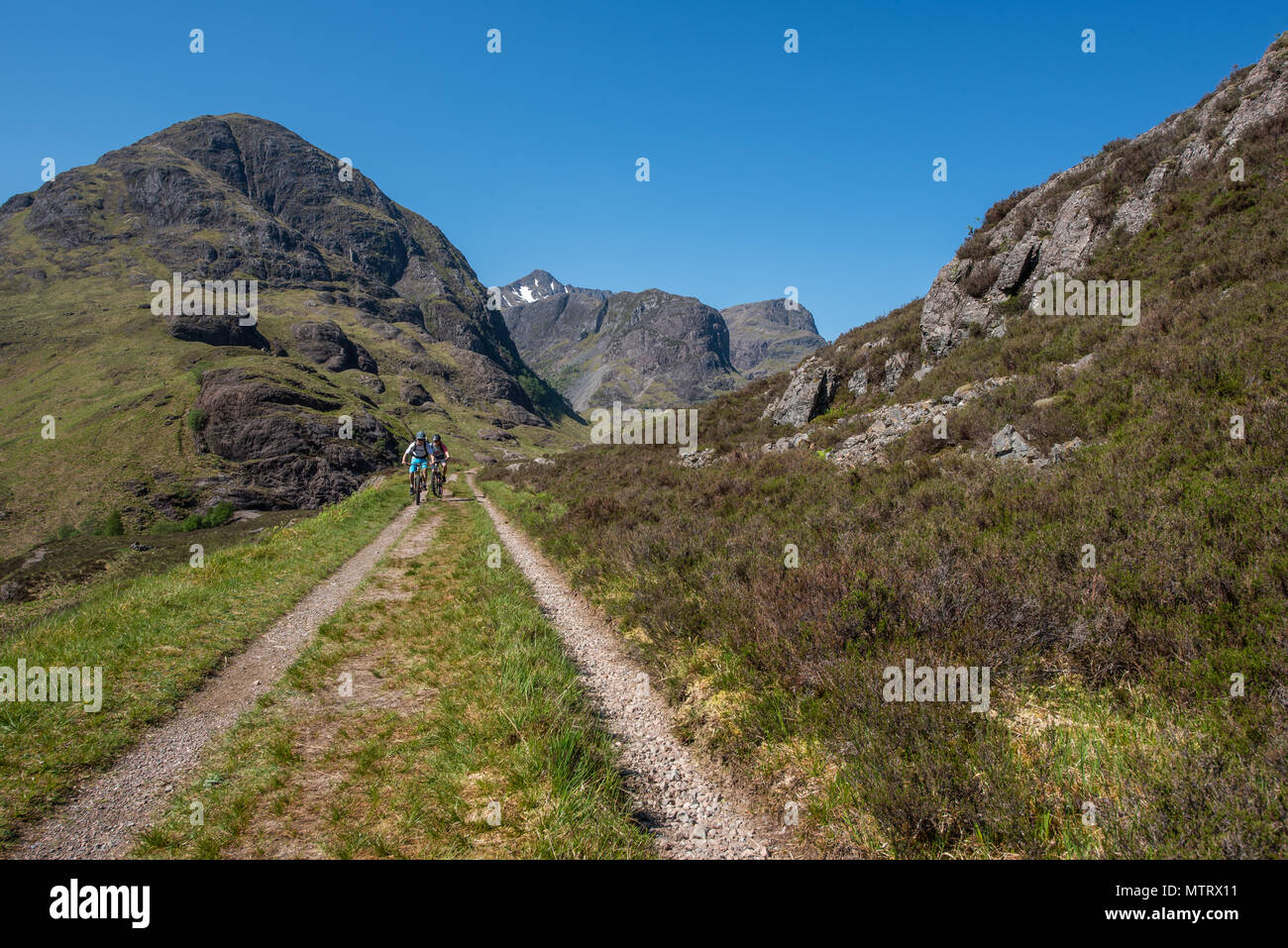 I ciclisti sulla vecchia strada militare sulle colline sopra la nuova strada che corre attraverso Glencoe con la struttura ad albero delle sorelle in background Foto Stock