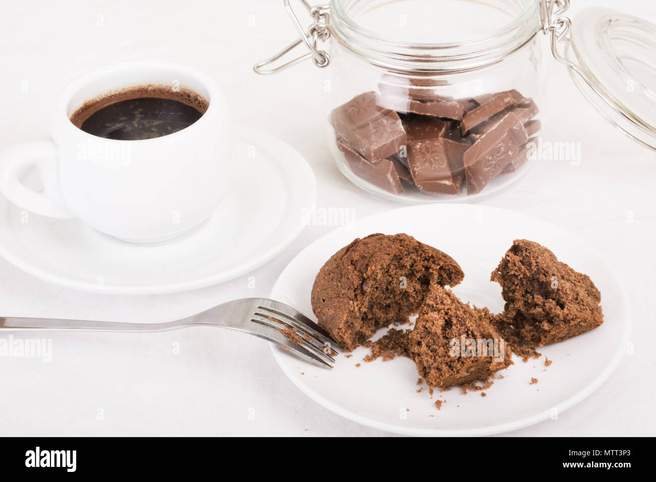 Muffin al cioccolato rotto aperto su una piastra, caffè nero e pezzi di cioccolato in un vaso. Messa a fuoco selettiva Foto Stock