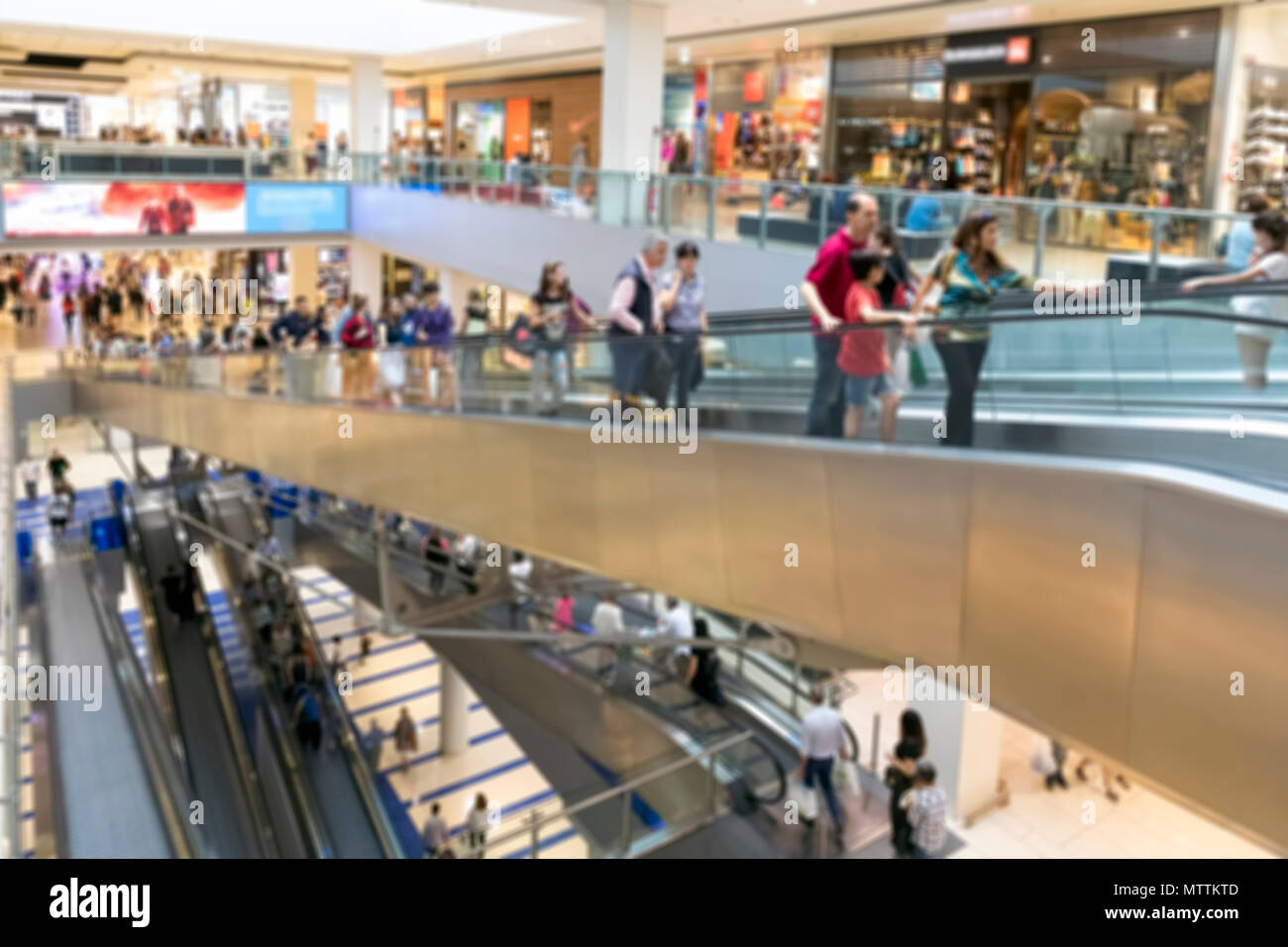Le persone andare a fare shopping all'interno del centro commerciale. Gli spazi con i vari negozi sono sviluppate su diversi piani collegati da lunghe scale mobili. sfocato Foto Stock